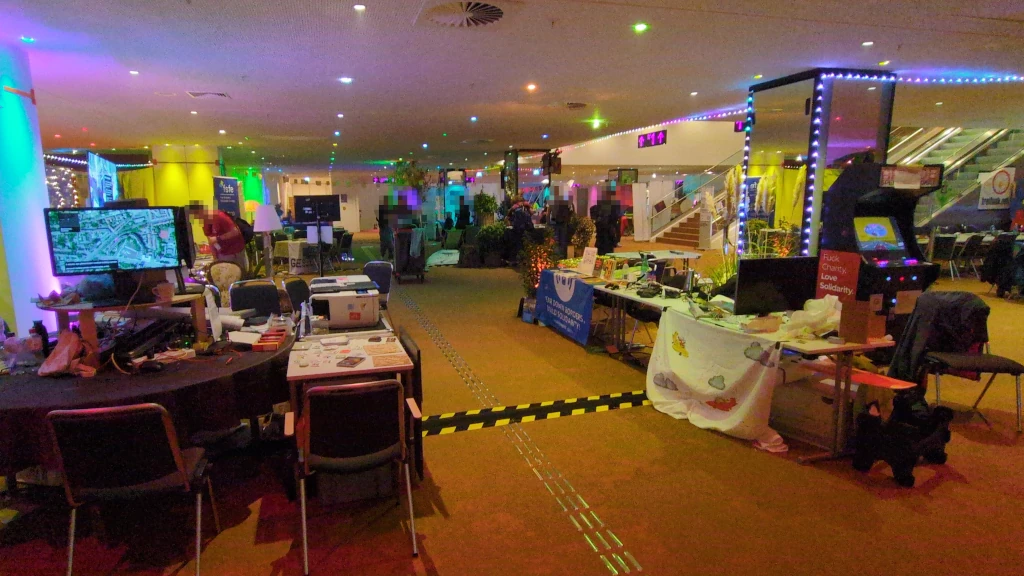Bunt beleuchtete Gänge mit Tischen voller Infomaterial, Banner, Lichterketten, Bildschirme.